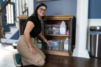 Lauren kneeling, smiling, and placing organizational bin in craft supplies cabinet
